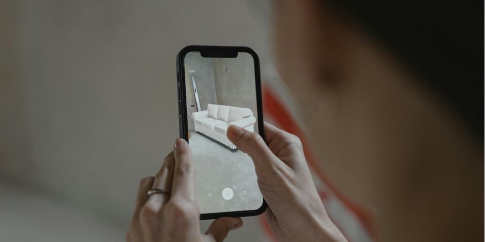 Eine Person hat ein Smartphone in der Hand und platziert auf dessen Display n in den Raum projeziertes Sofa. Bild Quelle: pexels.com