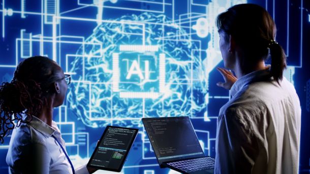 Zwei Personen stehen mit Tablet und Laptop in der Hand vor einer abstrakten Darstellung mit der Abkürzung AI in der Mitte. (Quelle: Storyblocks)