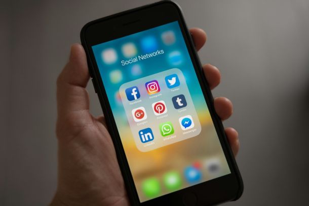 Eine Hand die ein altes iPhone hält, das Display zeigt den Home Bildschirm mit dem Ordner Social Networks geöffnet, darin befinden sich App Icons von Facebook, Instagram und mehr.